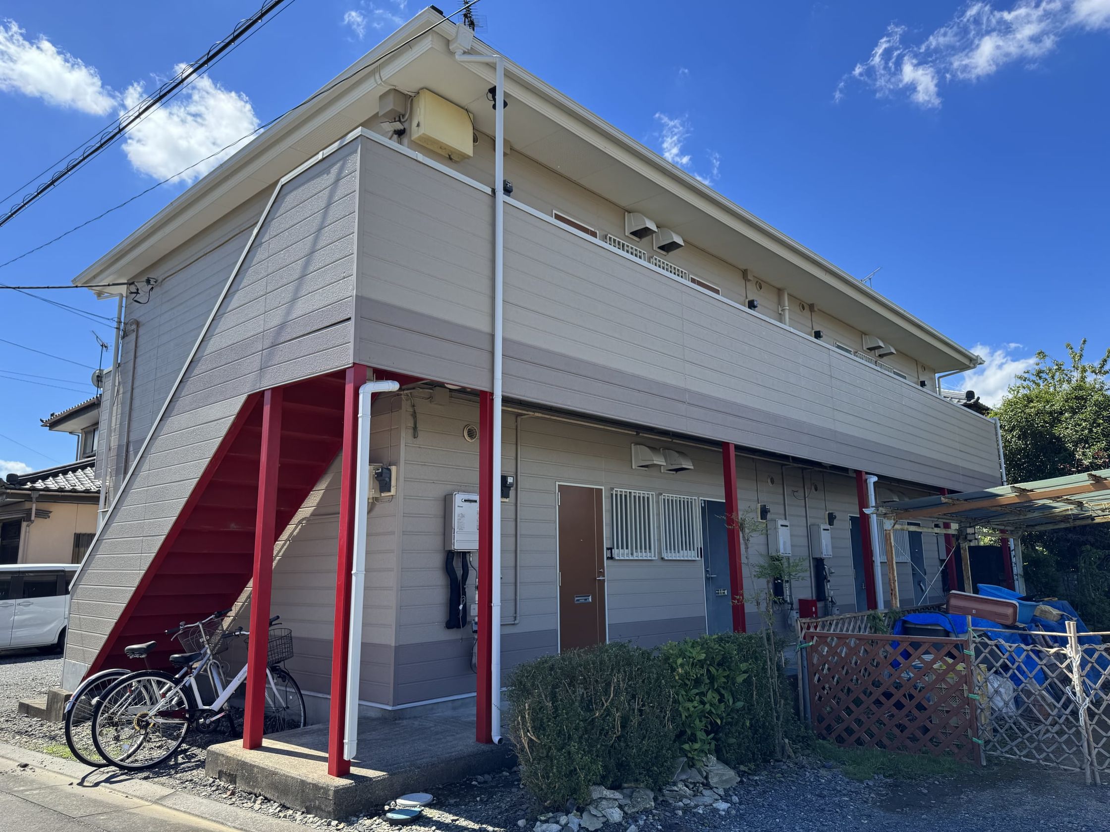 建物の玄関側の外観。1 階に各部屋の玄関ドアが並び、手前に植え込み